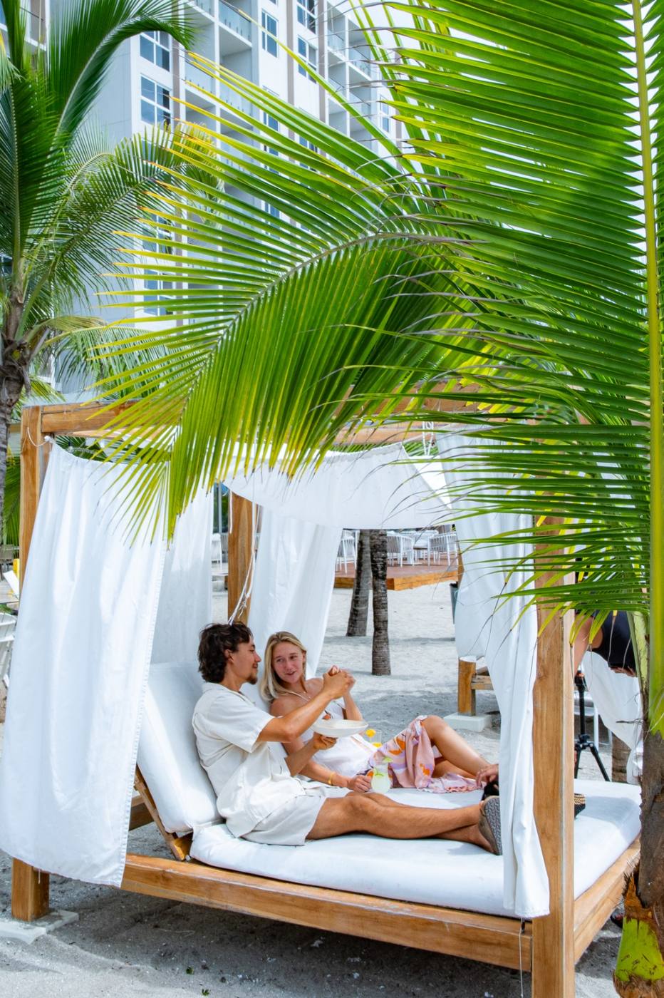 Couple relaxing in a beach cabana with white drapes at Playa Caracol