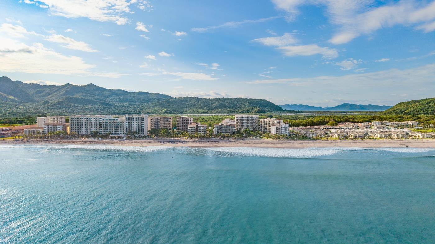 Aerial panoramic view of Playa Caracol resort showing the beach, ocean, and mountains
